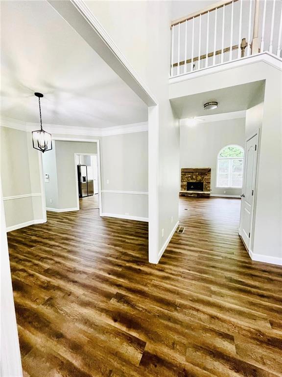 entrance foyer featuring crown molding, dark wood-style flooring, a fireplace, baseboards, and an inviting chandelier