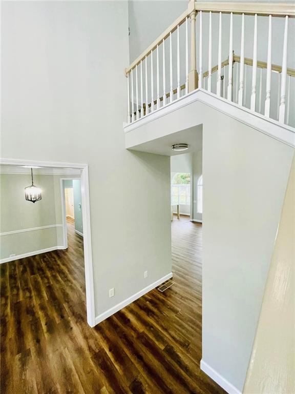 hall with dark wood-type flooring, visible vents, a towering ceiling, and baseboards