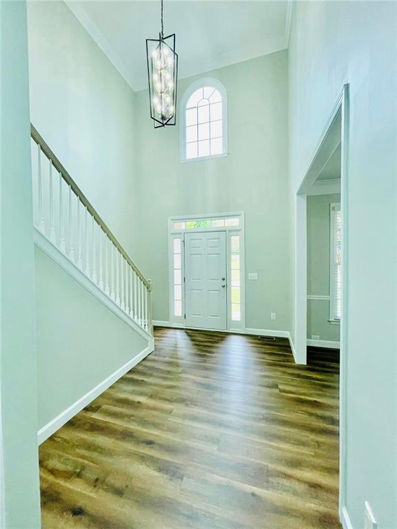 entrance foyer with baseboards, a towering ceiling, dark wood-style floors, ornamental molding, and a chandelier