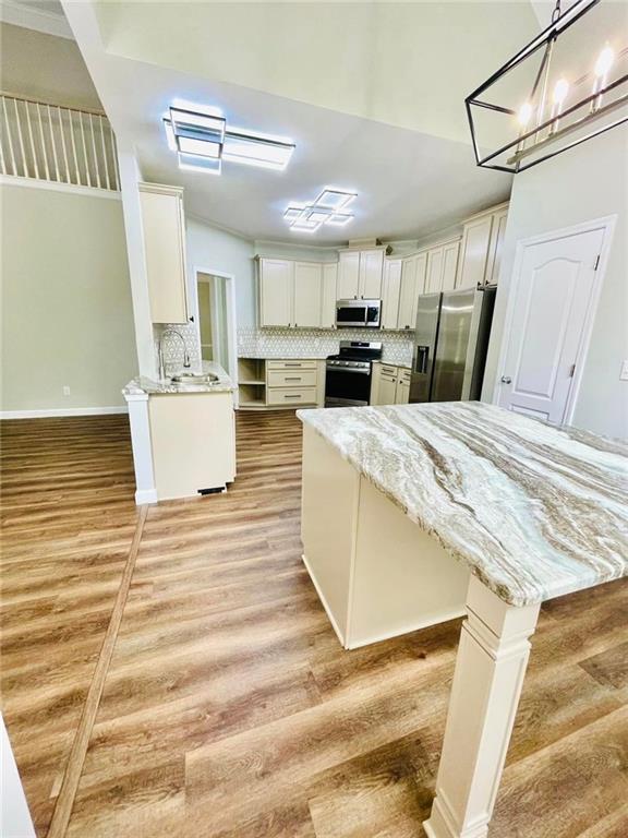 kitchen featuring light wood finished floors, white cabinets, decorative backsplash, hanging light fixtures, and stainless steel appliances