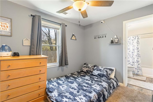 carpeted bedroom with visible vents, ensuite bathroom, and a ceiling fan