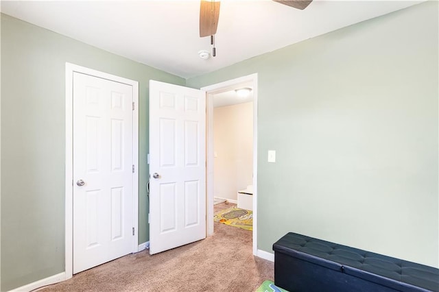 interior space featuring baseboards, light colored carpet, and a ceiling fan