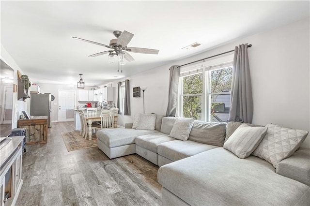 living room with visible vents, baseboards, light wood-style floors, and ceiling fan