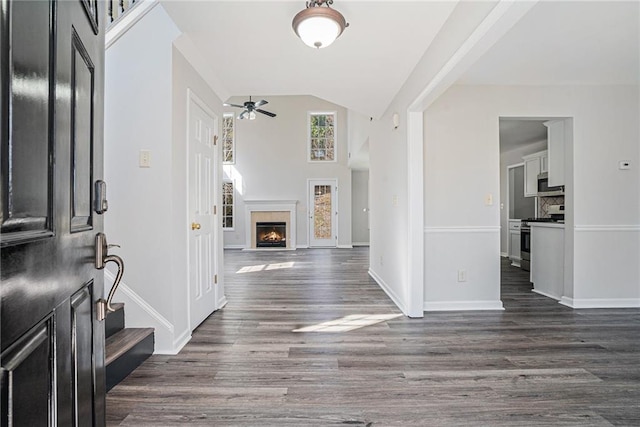 entryway with baseboards, dark wood finished floors, a warm lit fireplace, ceiling fan, and stairs