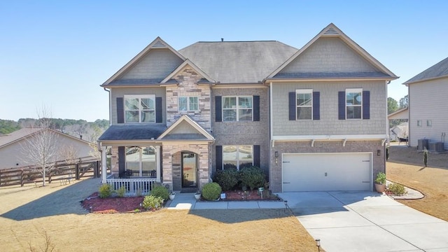 craftsman-style home with fence, covered porch, concrete driveway, a garage, and stone siding