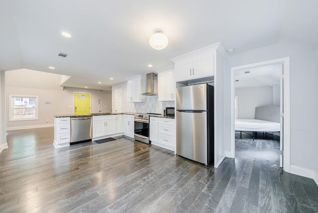 kitchen featuring wall chimney range hood, appliances with stainless steel finishes, backsplash, white cabinets, and kitchen peninsula