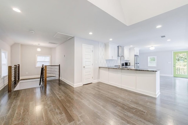 kitchen with white cabinetry, wood-type flooring, kitchen peninsula, white fridge, and decorative backsplash