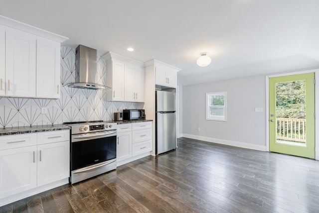 kitchen featuring white cabinetry, stainless steel appliances, decorative backsplash, dark stone counters, and wall chimney exhaust hood