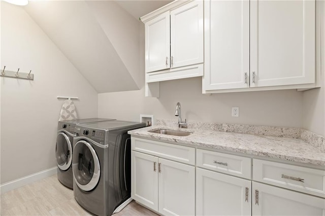 laundry area featuring cabinets, sink, light wood-type flooring, and washer and dryer