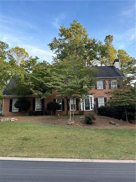 colonial-style house with brick siding, a chimney, and a front lawn