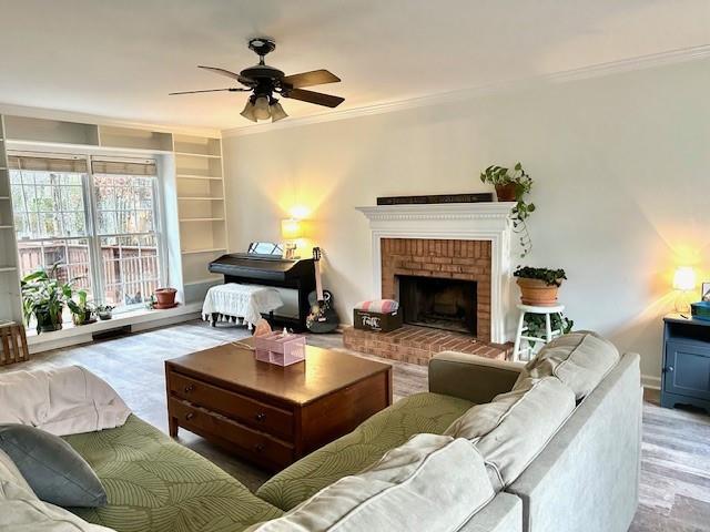 living room featuring built in features, baseboards, a fireplace, ceiling fan, and crown molding