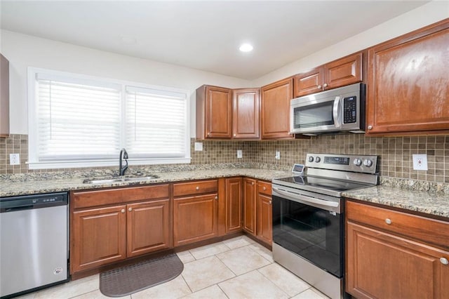 kitchen with stainless steel appliances, light stone countertops, brown cabinetry, and a sink