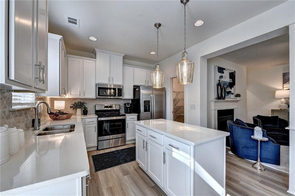 kitchen with stainless steel appliances, a kitchen island, sink, pendant lighting, and white cabinetry