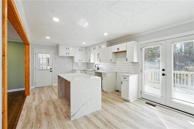 kitchen with a kitchen island, sink, white cabinets, light stone counters, and french doors