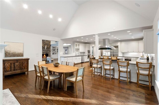 dining space featuring dark hardwood / wood-style flooring, high vaulted ceiling, sink, and decorative columns