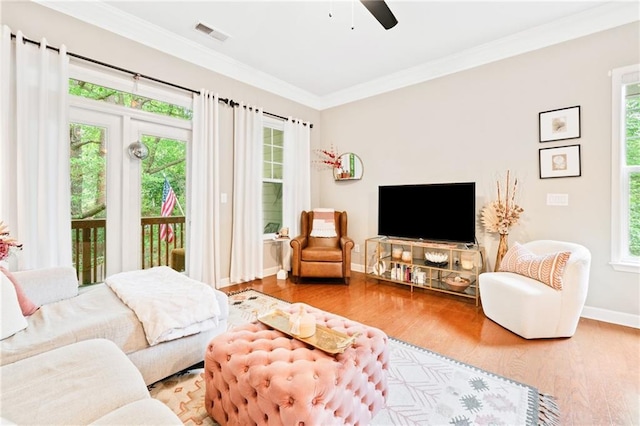 living area with healthy amount of natural light, a ceiling fan, wood finished floors, baseboards, and crown molding