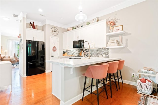 kitchen featuring black appliances, a peninsula, a breakfast bar area, ornamental molding, and white cabinets