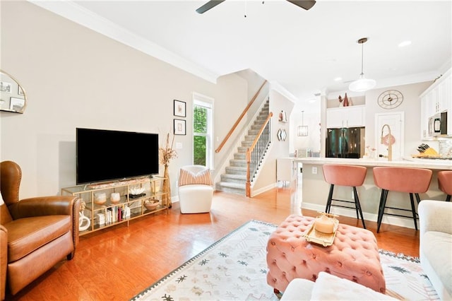living area with ornamental molding, stairs, a ceiling fan, light wood-type flooring, and baseboards