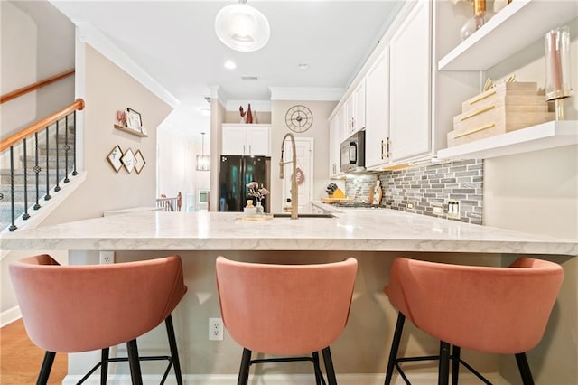kitchen featuring a peninsula, tasteful backsplash, white cabinets, freestanding refrigerator, and crown molding