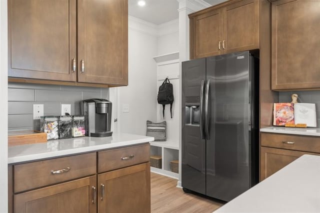 kitchen featuring stainless steel fridge, light countertops, ornamental molding, and light wood-style floors