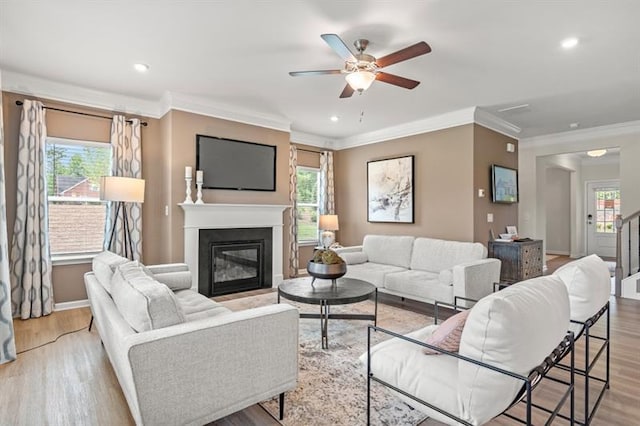 living room with crown molding, a ceiling fan, baseboards, and a glass covered fireplace