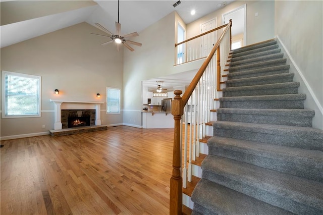 staircase with a fireplace, hardwood / wood-style flooring, high vaulted ceiling, and ceiling fan