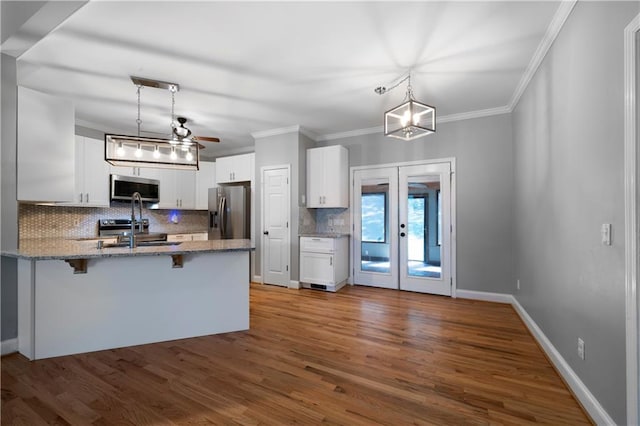 kitchen with a breakfast bar area, white cabinetry, hanging light fixtures, and appliances with stainless steel finishes