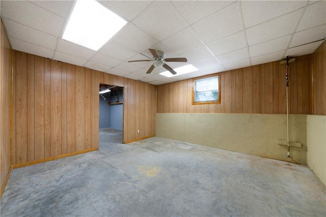 basement featuring a paneled ceiling, ceiling fan, and wooden walls