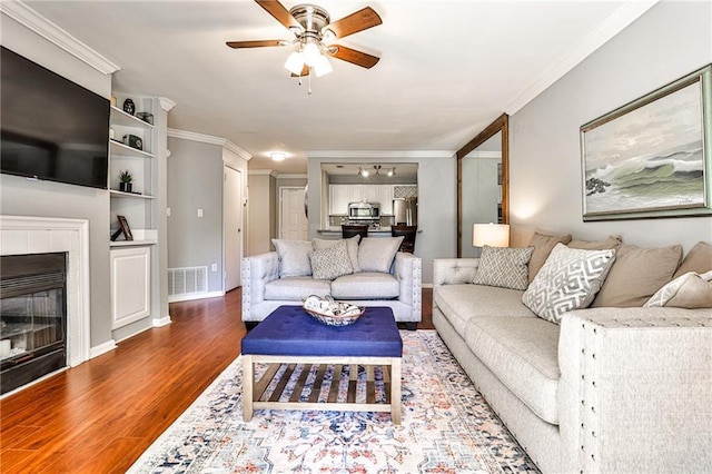 living room featuring a tile fireplace, wood-type flooring, ceiling fan, and crown molding