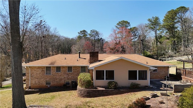 rear view of property with brick siding, a chimney, and a yard