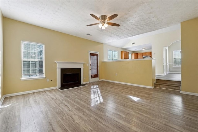 unfurnished living room featuring ceiling fan, plenty of natural light, a textured ceiling, and light wood-type flooring