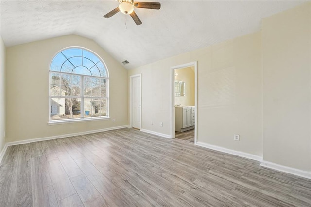 empty room with ceiling fan, vaulted ceiling, and light wood-type flooring