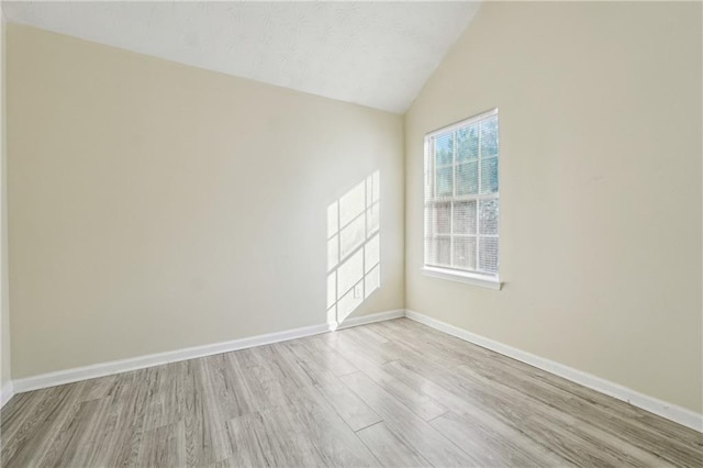 spare room with lofted ceiling and light hardwood / wood-style flooring