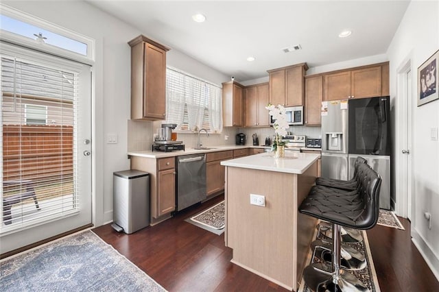 kitchen with a wealth of natural light, a center island, dark wood-type flooring, a kitchen breakfast bar, and appliances with stainless steel finishes