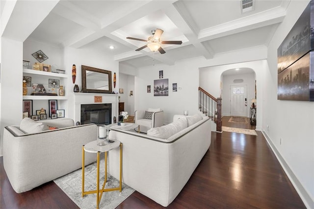 living room featuring dark hardwood / wood-style flooring, coffered ceiling, built in shelves, ceiling fan, and beamed ceiling