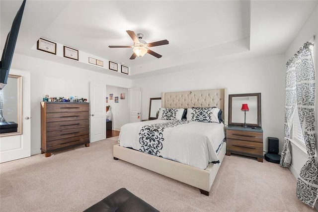 bedroom featuring light colored carpet, a raised ceiling, and ceiling fan