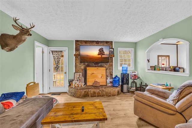 living room with a stone fireplace, a textured ceiling, and light hardwood / wood-style floors