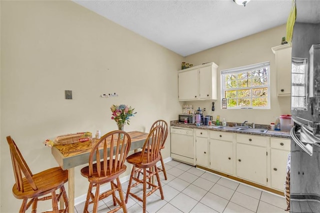 kitchen featuring sink, a textured ceiling, light tile patterned floors, dishwasher, and white cabinets