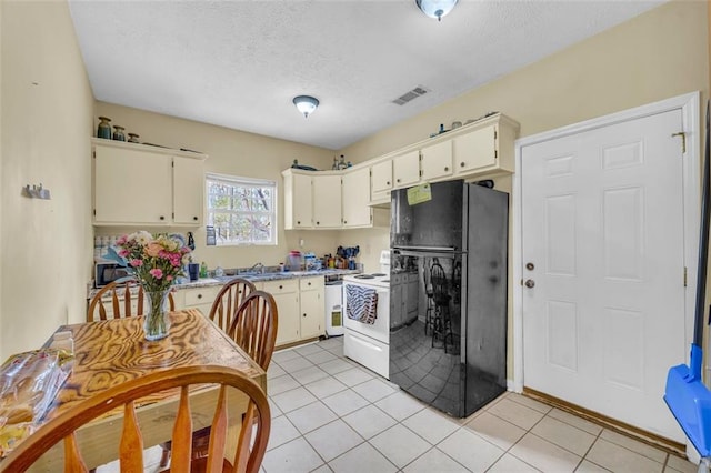 kitchen with black refrigerator, dishwasher, light tile patterned floors, cream cabinetry, and electric stove