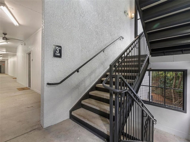 stairs featuring ceiling fan and concrete floors