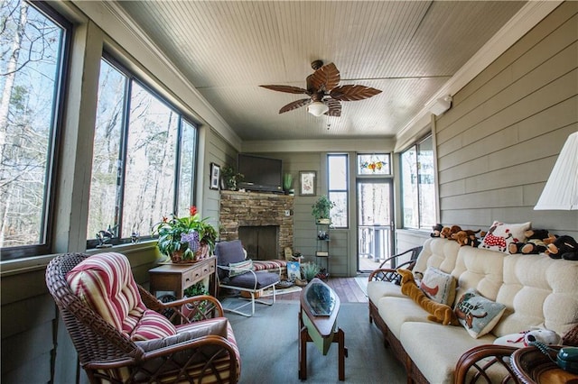 sunroom / solarium featuring ceiling fan, a healthy amount of sunlight, and a stone fireplace