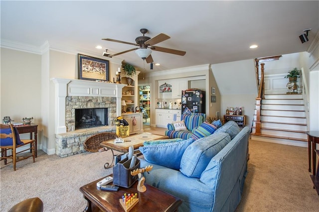 carpeted living room with a stone fireplace, ceiling fan, and ornamental molding