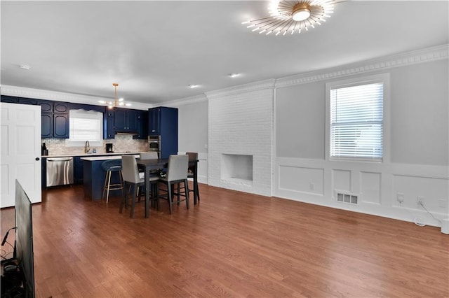 dining space with crown molding, sink, a brick fireplace, a notable chandelier, and wood-type flooring