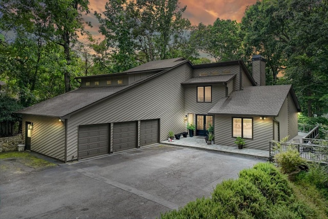 6144 Scott Dr, Flowery Branch, GA 30542 - mid-century inspired home featuring a chimney, roof with shingles, driveway, view of wooded area, and a garage
