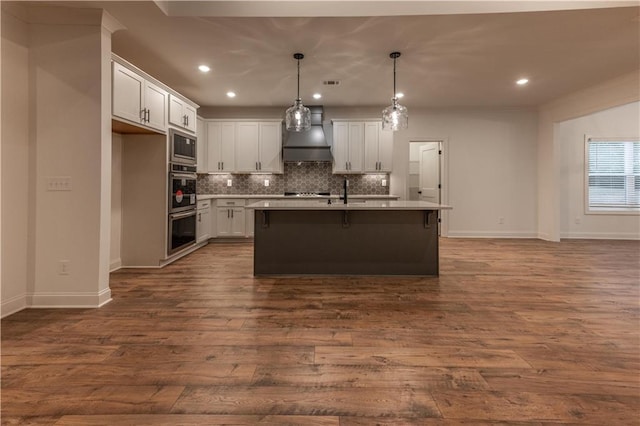 kitchen with white cabinets, hardwood / wood-style floors, a center island with sink, and premium range hood