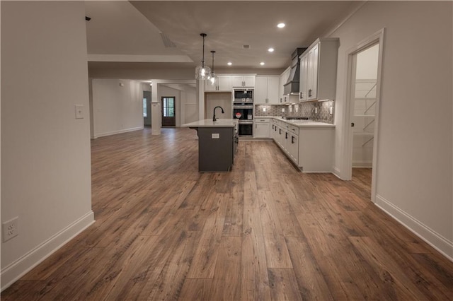 kitchen with appliances with stainless steel finishes, dark hardwood / wood-style flooring, decorative light fixtures, a center island with sink, and white cabinets