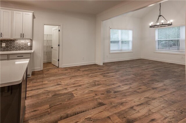 unfurnished dining area with a chandelier, crown molding, and dark wood-type flooring