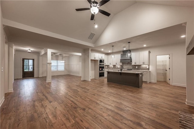 kitchen featuring custom exhaust hood, pendant lighting, a center island with sink, white cabinets, and hardwood / wood-style floors