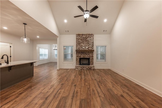 unfurnished living room featuring high vaulted ceiling, a brick fireplace, ceiling fan, and dark wood-type flooring