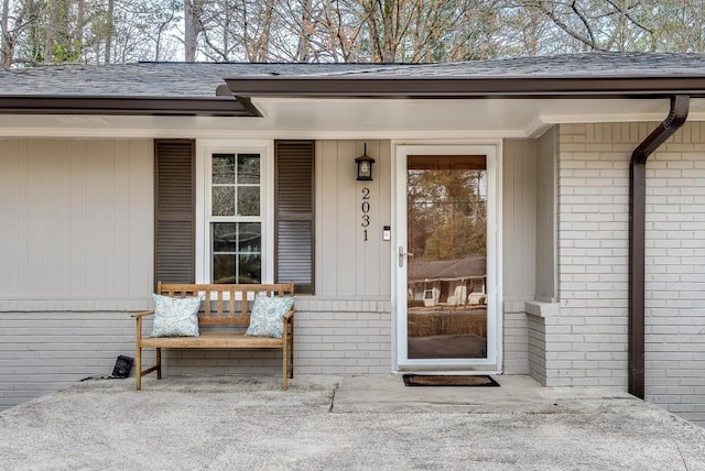 property entrance with brick siding, a porch, and roof with shingles